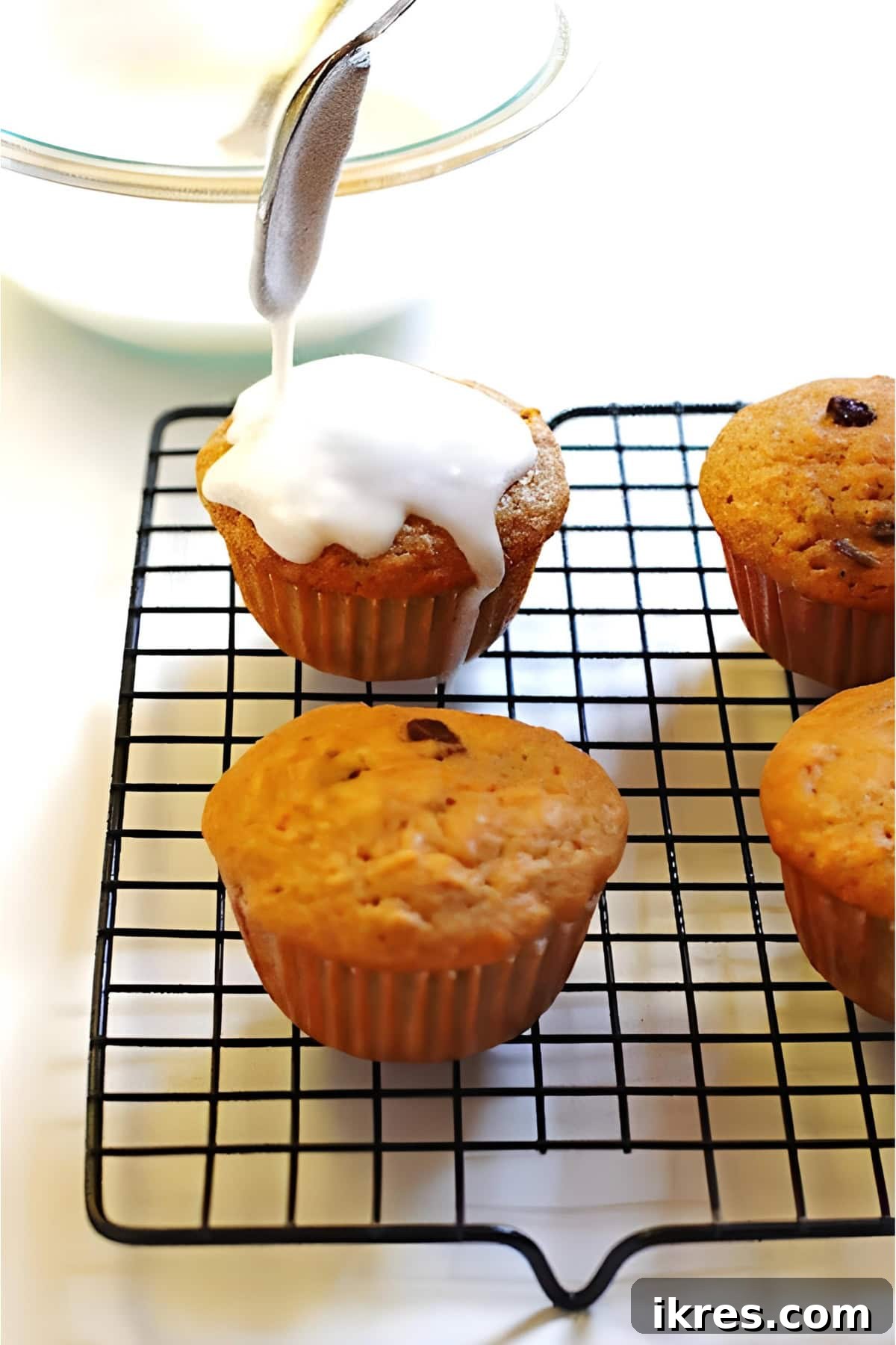 Perfectly Spiced Carrot Cake Muffins with Cream Cheese Glaze 7 A spoon drizzling glaze over carrot cake muffins.