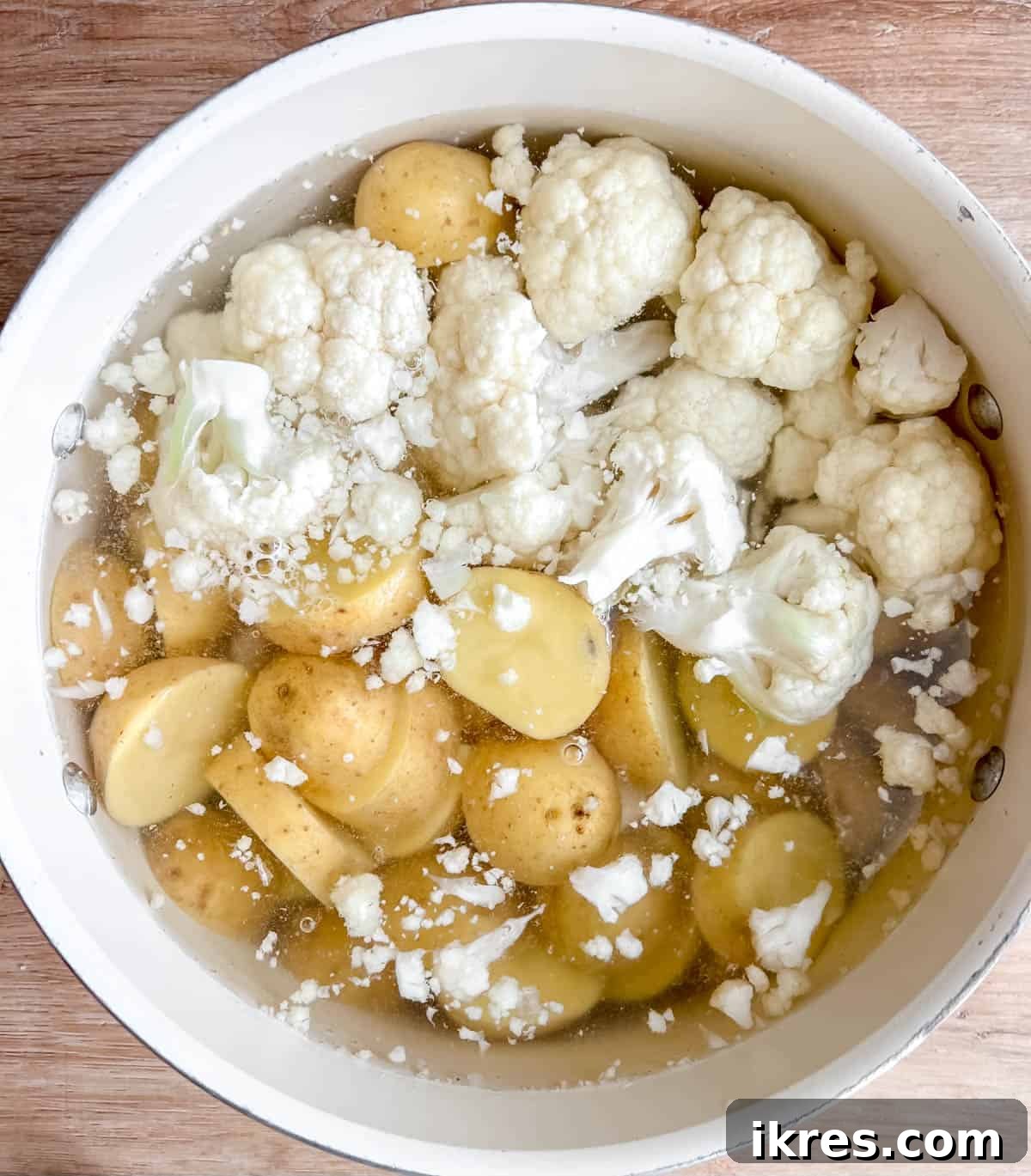Sliced potatoes and cauliflower florets boiling in a large pot of water on the stovetop.