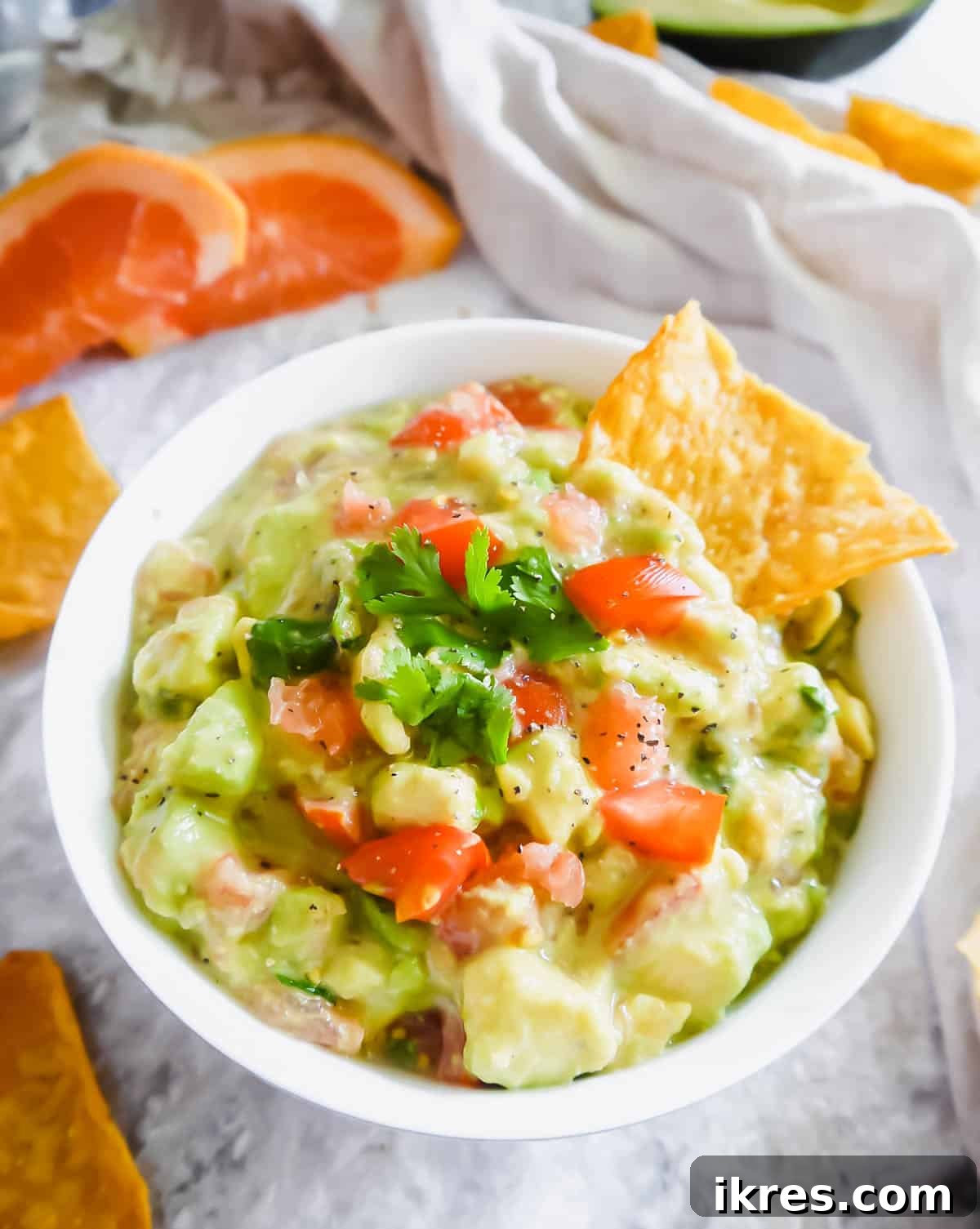 Zesty citrus guacamole in a bowl with a tortilla chip dipped inside, showcasing its vibrant texture.