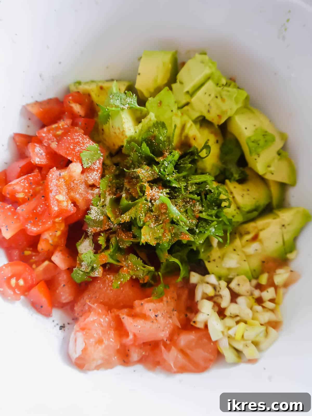 A colorful array of fresh ingredients including avocados, grapefruit, onion, garlic, cilantro, lime, and tomatoes, laid out for guacamole preparation.