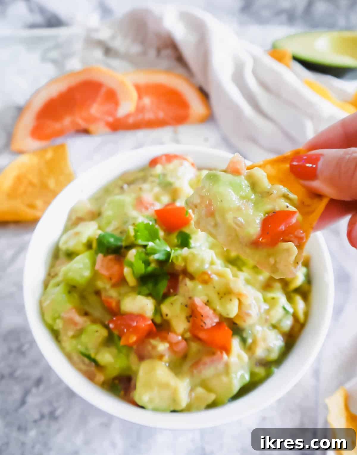 A hand dipping a crispy chip into a bowl of creamy Grapefruit Guacamole, showing its appealing texture.