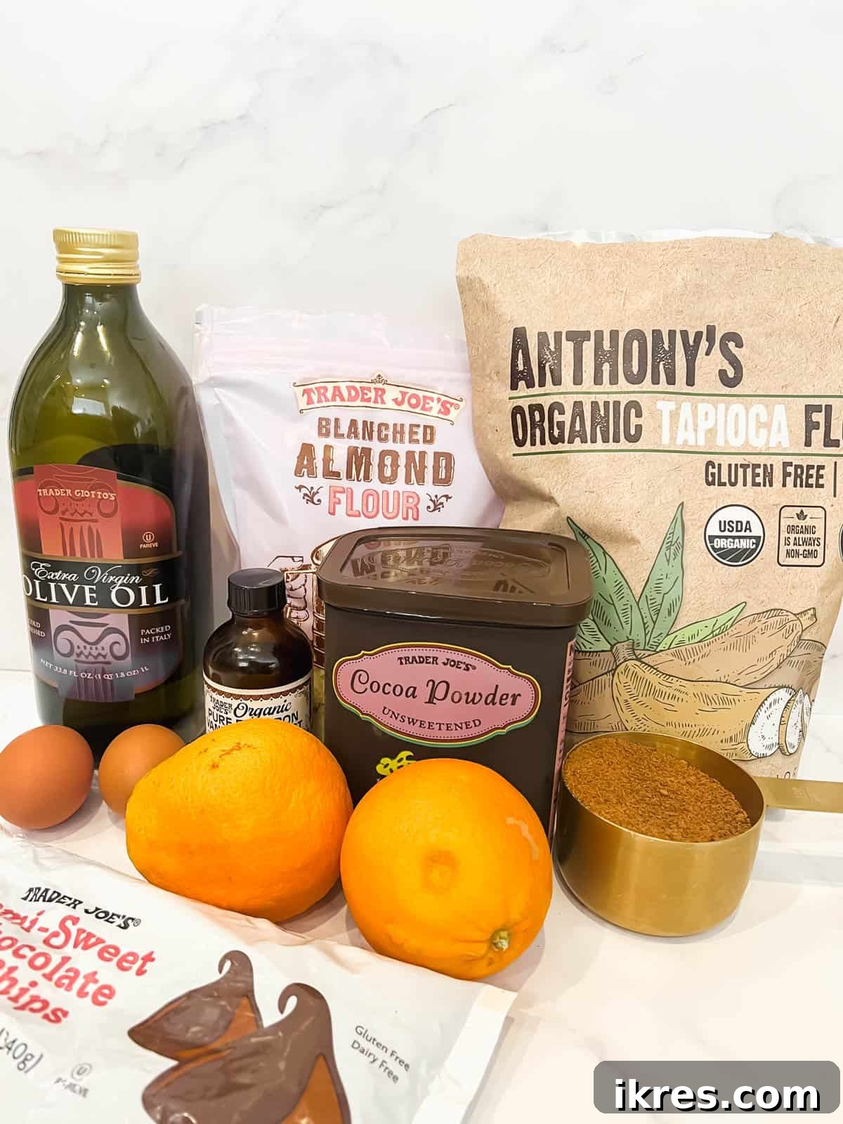 A flat lay photograph displaying all the fresh and dry ingredients required for making chocolate orange brownies, including oranges, flours, cocoa, and chocolate chips.