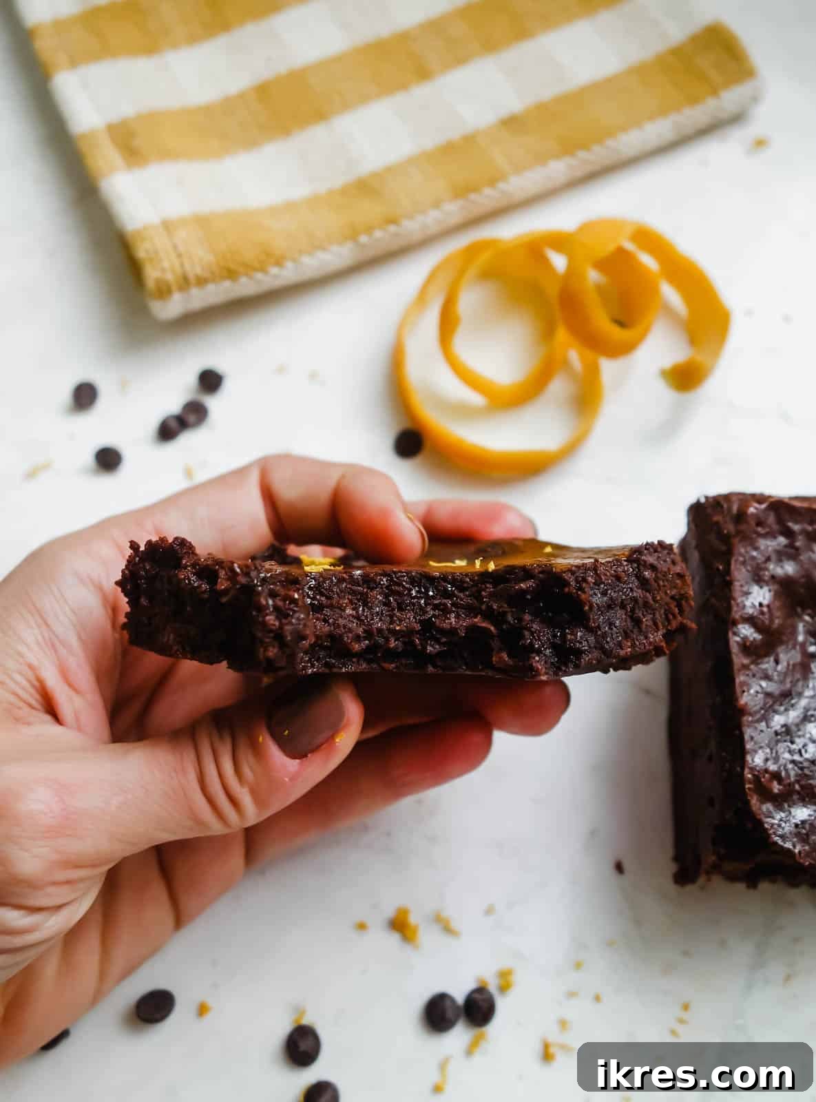 A close-up photo of a chocolate orange brownie with a bite taken out, revealing its rich, fudgy interior and speckled orange zest.