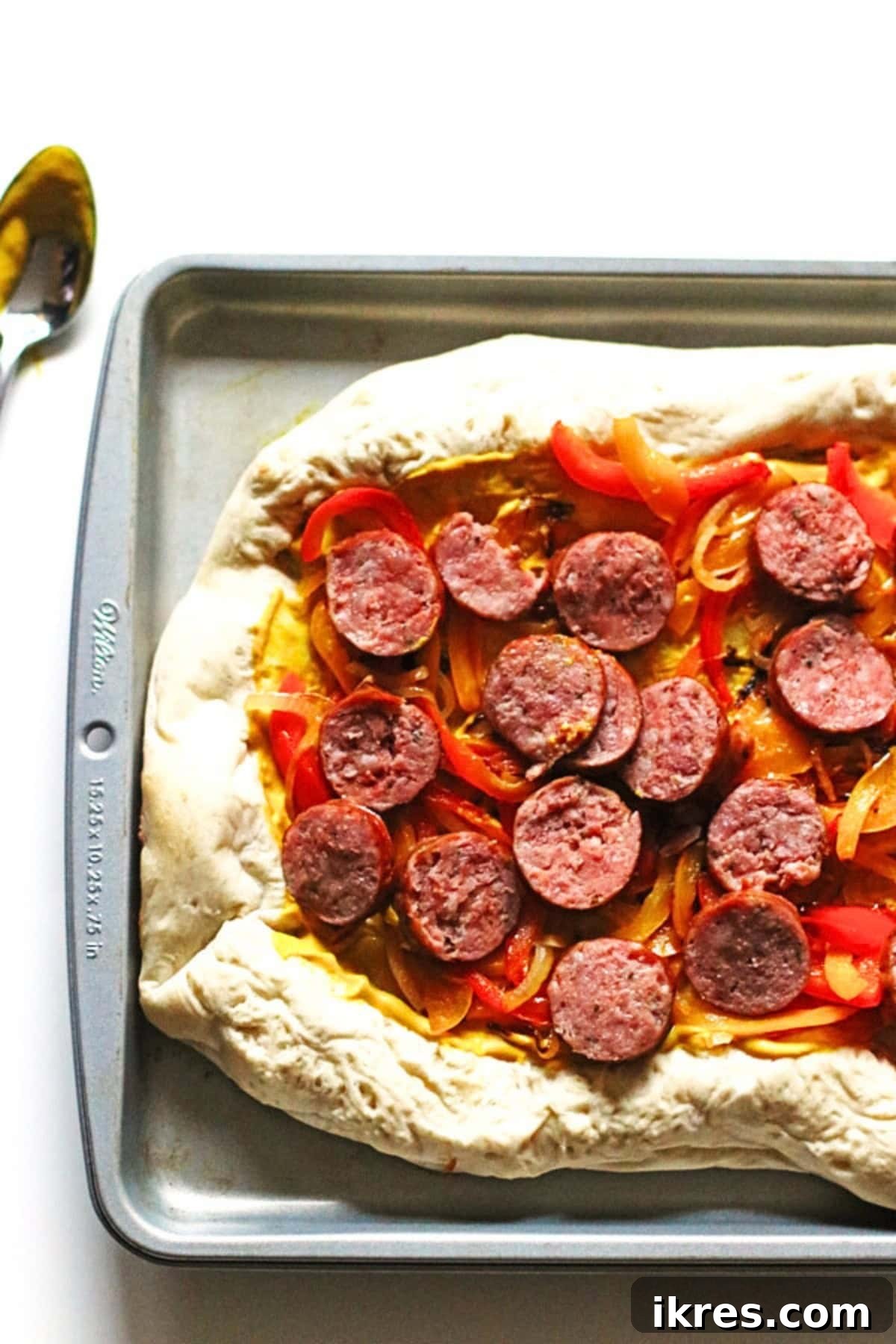 Supreme Pizza Perfection 5 Peppers, onion and cooked Polish sausage placed on pizza dough on a baking pan