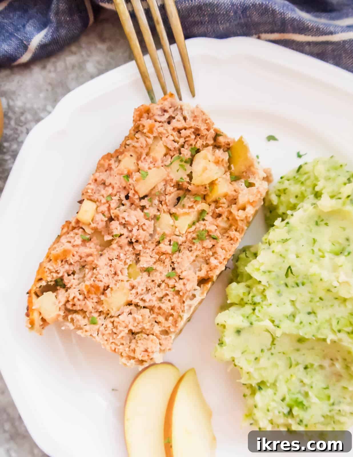 A perfectly sliced portion of turkey apple meatloaf on a clean white plate, revealing its texture and apple pieces.