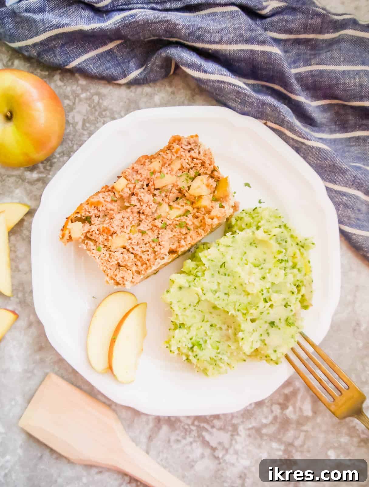 A beautiful slice of paleo meatloaf, visibly showing pieces of apple and herbs, served on a plate with fresh greens.