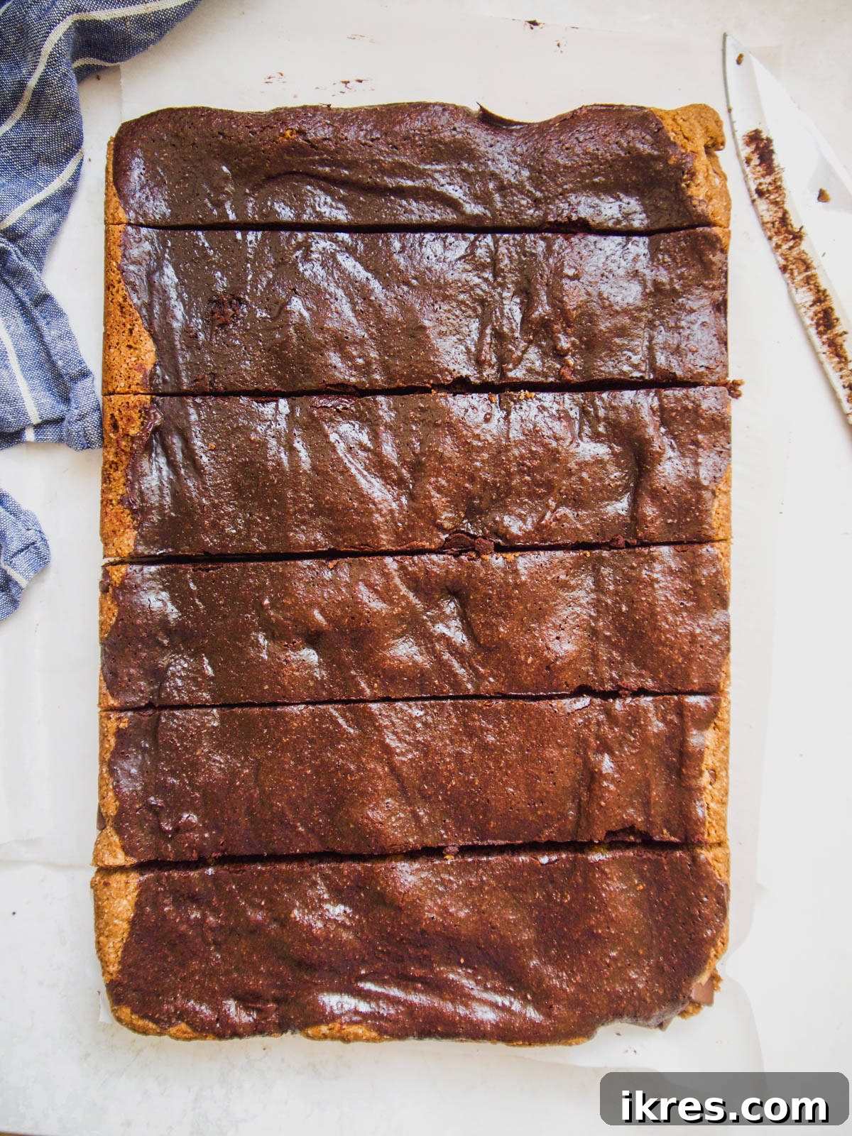 A sharp knife slicing through a sheet of freshly baked Paleo brownie cookie bars.