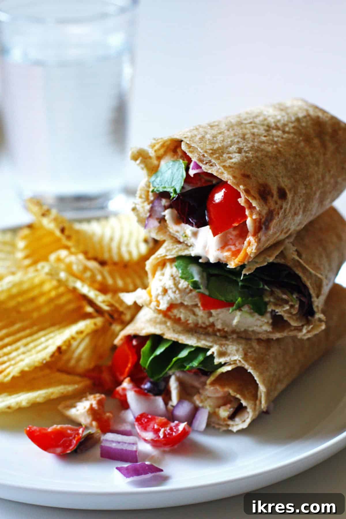 Loaded Ranch Chicken Wraps 4 A stack of three chicken wraps on a plate, served with tomatoes, red onion, and potato chips.