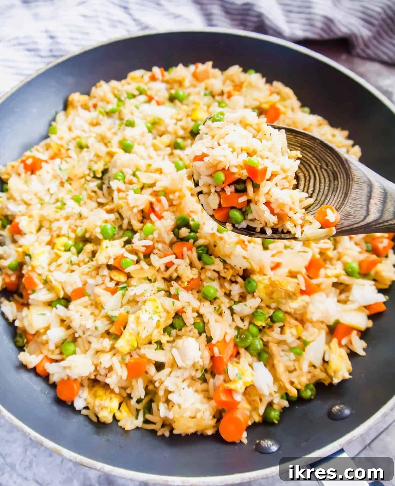 A serving spoon lifts a generous portion of freshly made coconut aminos fried rice from a sizzling frying pan, showcasing the vibrant colors of the vegetables and fluffy rice.
