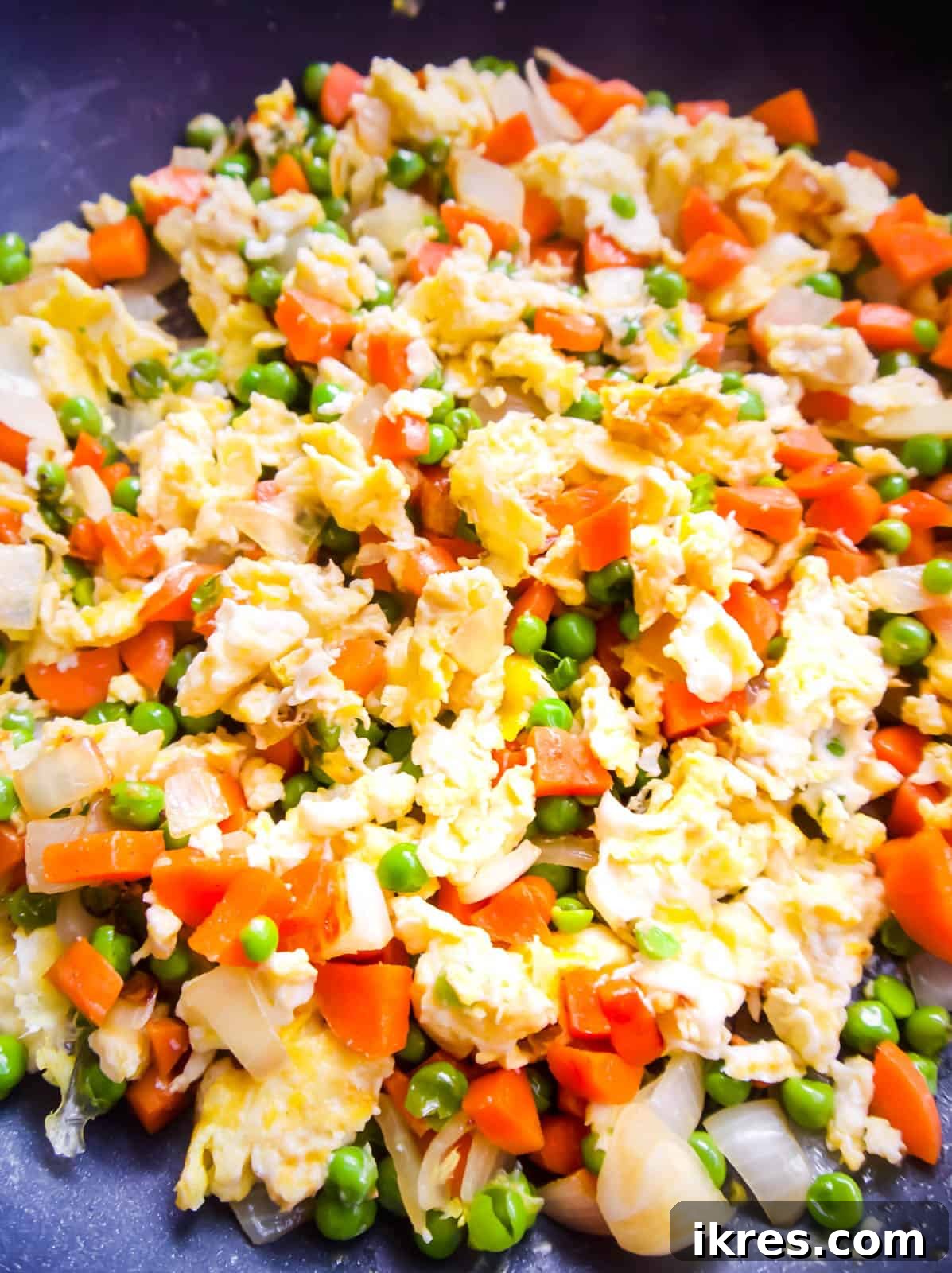 A close-up shot of the frying pan shows the scrambled eggs and sautéed vegetables now fully mixed together, creating a colorful and inviting base for the fried rice.