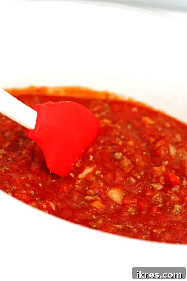 Beyaz bir yavaş tencerede ev yapımı spagetti sosu bir spatula ile karıştırılıyor.