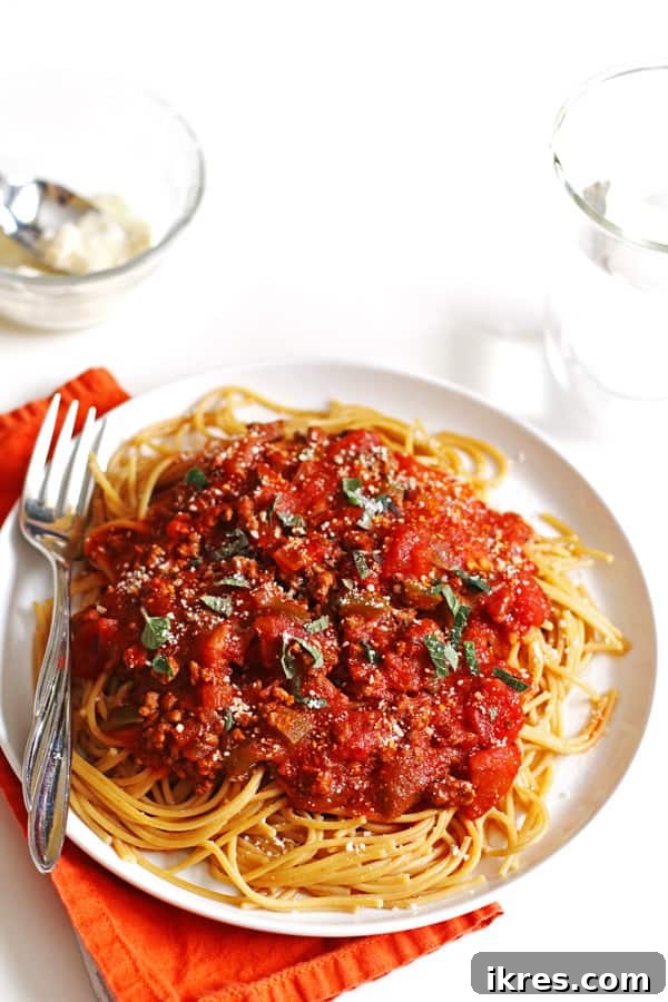 Soslu spagetti tabağı ve bir çatal. Yanında küçük bir kase rendelenmiş parmesan peyniri ve bir kaşık bulunuyor.