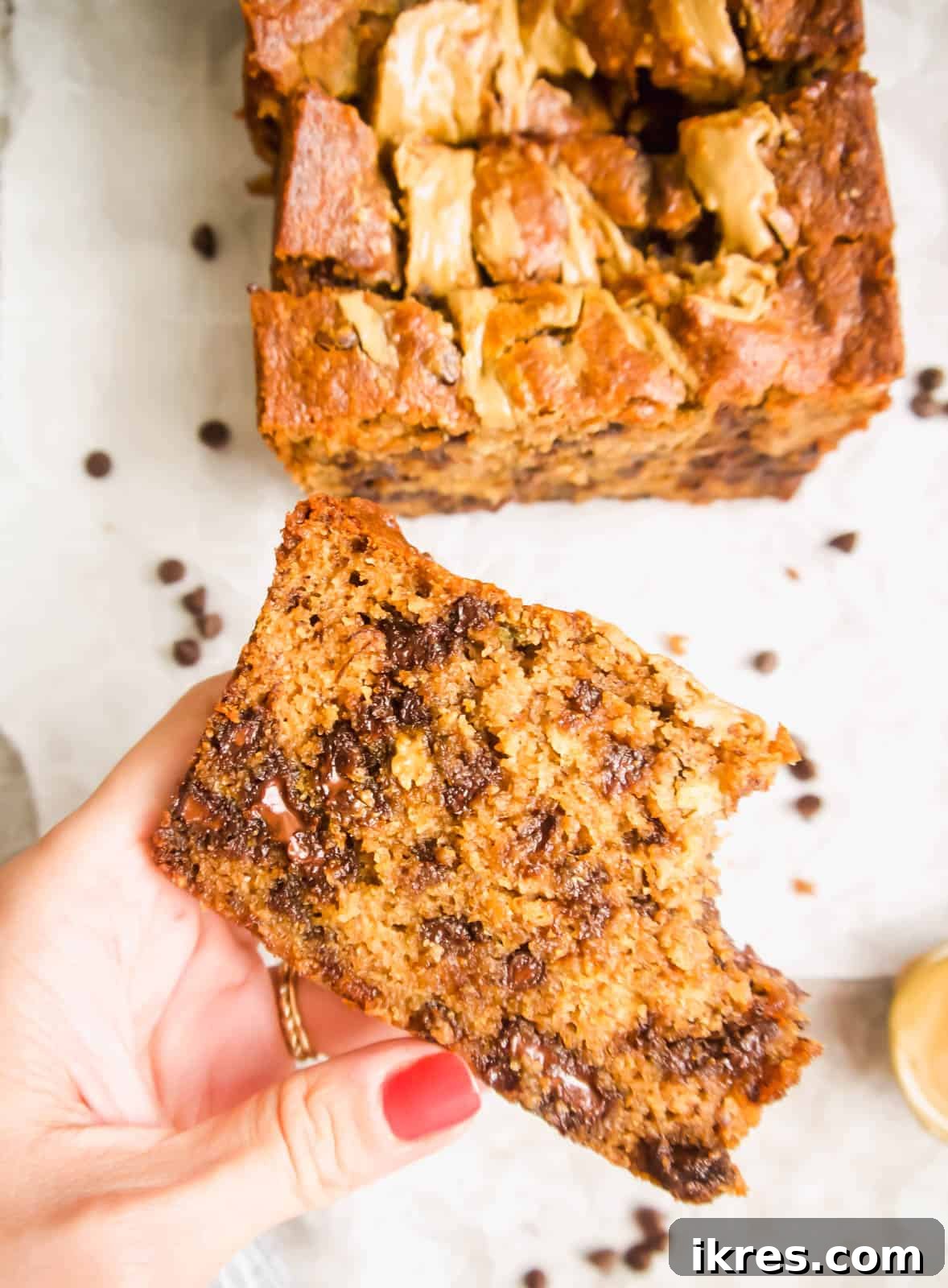 A hand holding a generous slice of Sunflower Seed Butter and Chocolate Chip Banana Bread, showcasing its thickness and inviting texture.