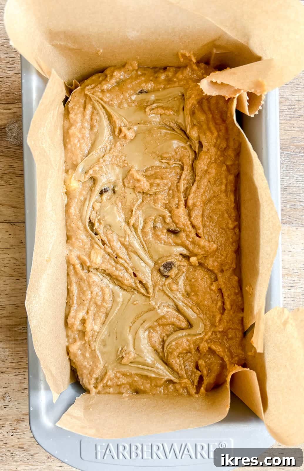 Banana bread batter in a loaf pan, with sunflower butter drizzled on top, ready for swirling.