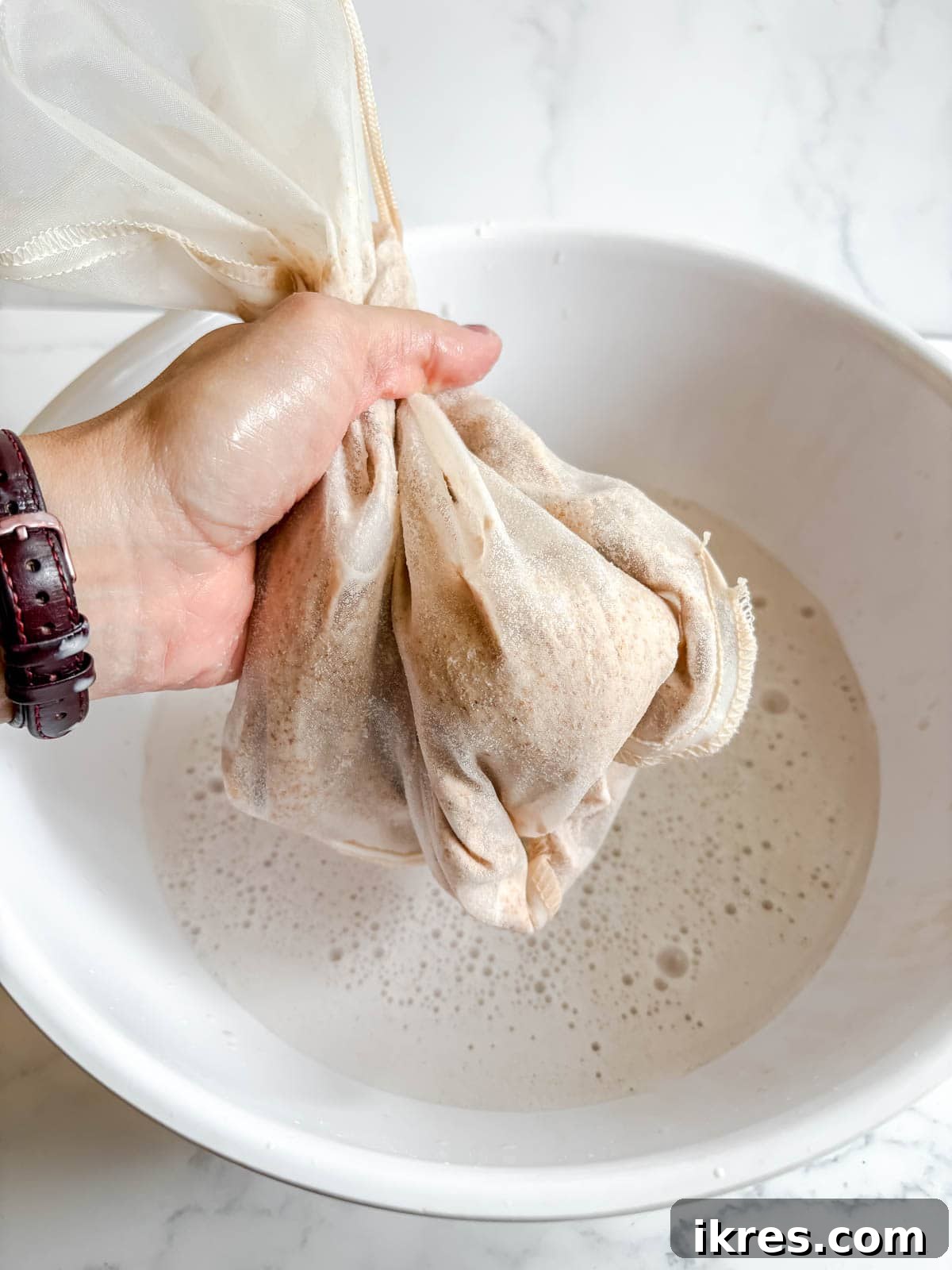 Homemade Vegan Strawberry Almond Milk 11 Hand squeezing the nut milk bag to extract almond milk.