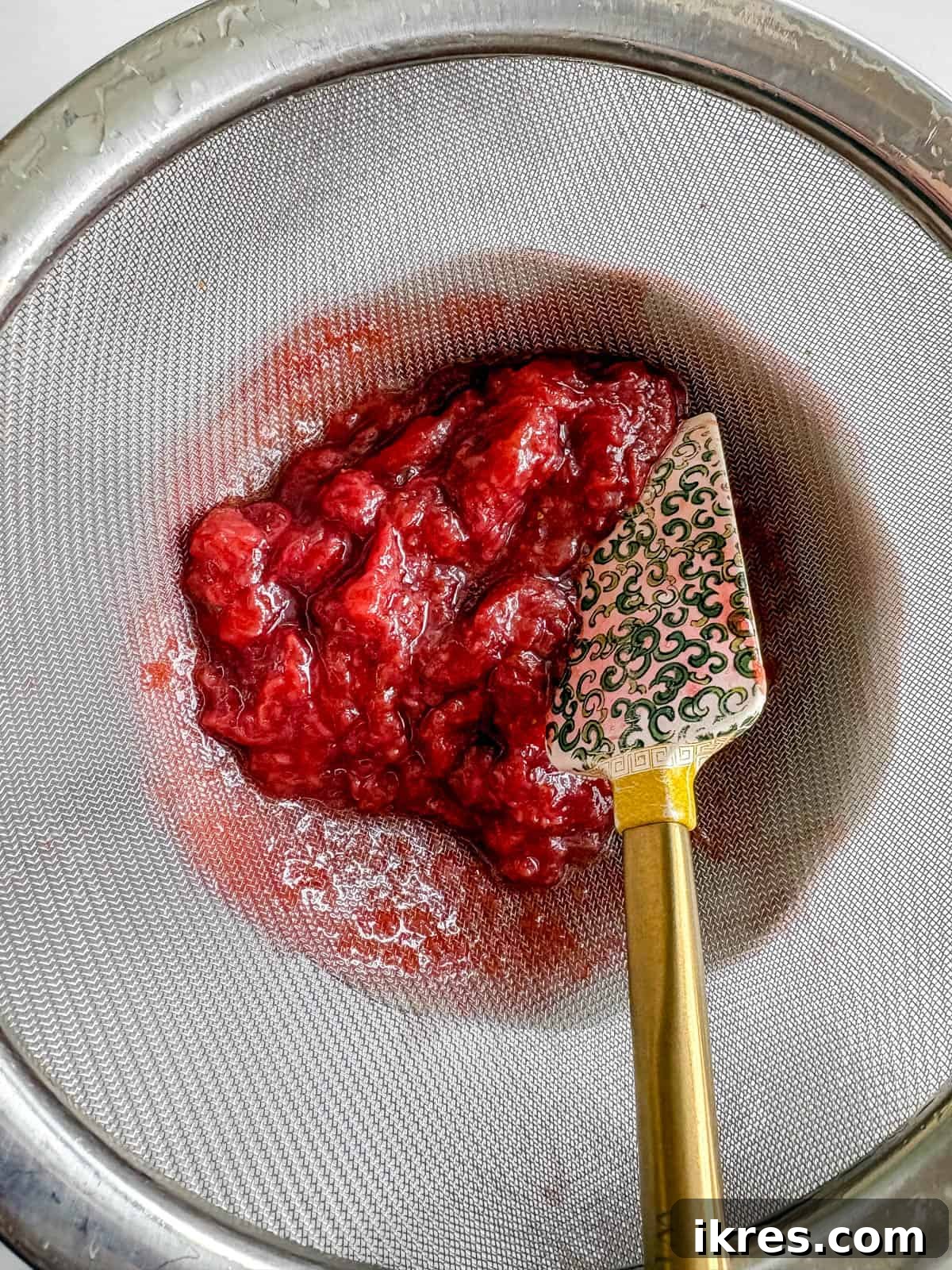 Homemade Vegan Strawberry Almond Milk 6 Straining the cooked strawberry pulp from the syrup using a fine mesh strainer.