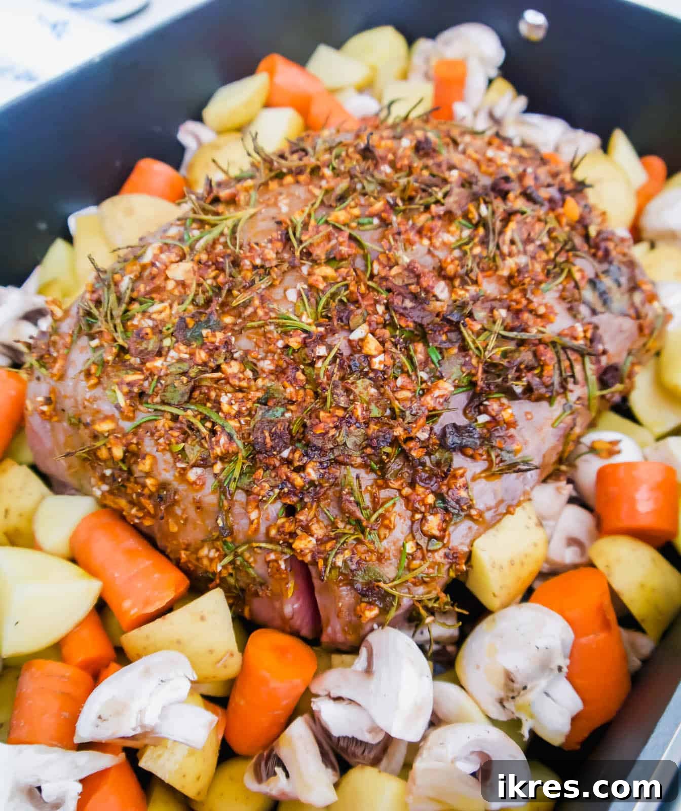 Savory Garlic Herb Shoulder Roast 6 Hearty potatoes, carrots, and mushrooms arranged around the partially cooked heart of clod roast in the pan.