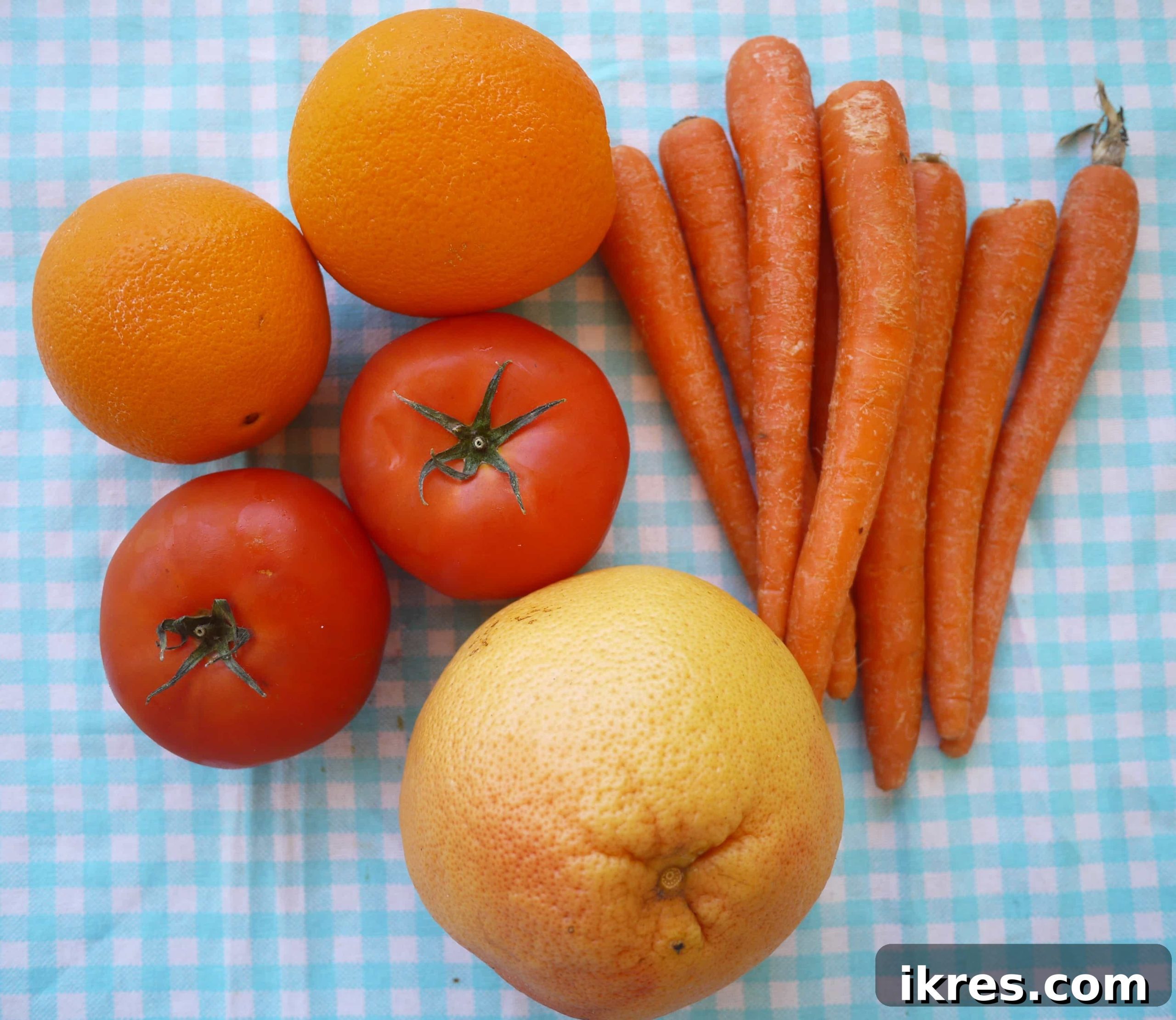 Fresh ingredients laid out on a table, including carrots, tomatoes, oranges, and grapefruit, ready for juicing.