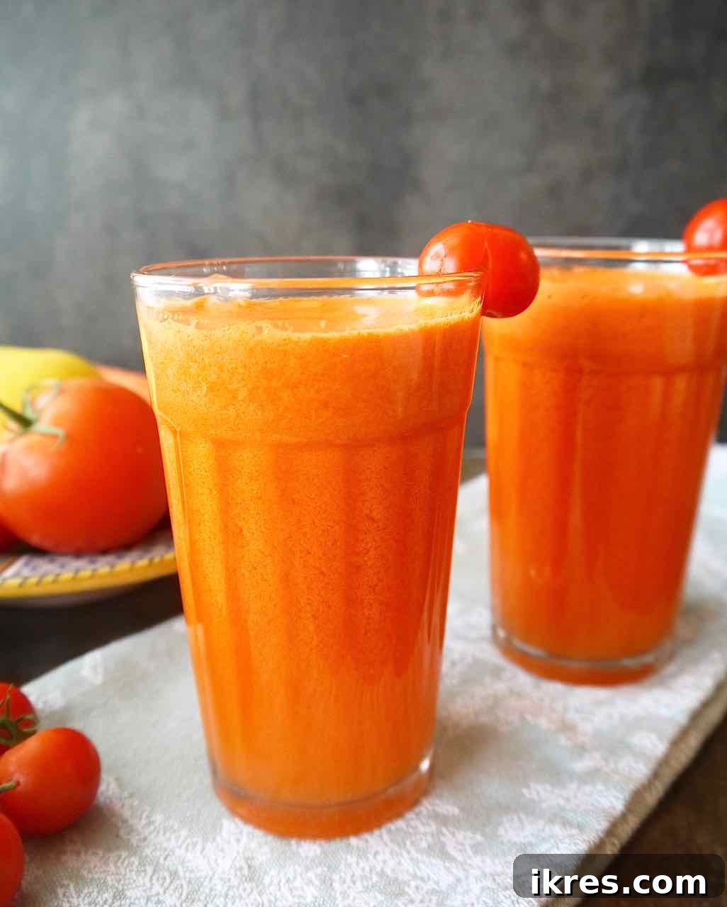 Two glasses of vibrant tomato carrot juice, garnished with a slice of fresh tomato on the rim.