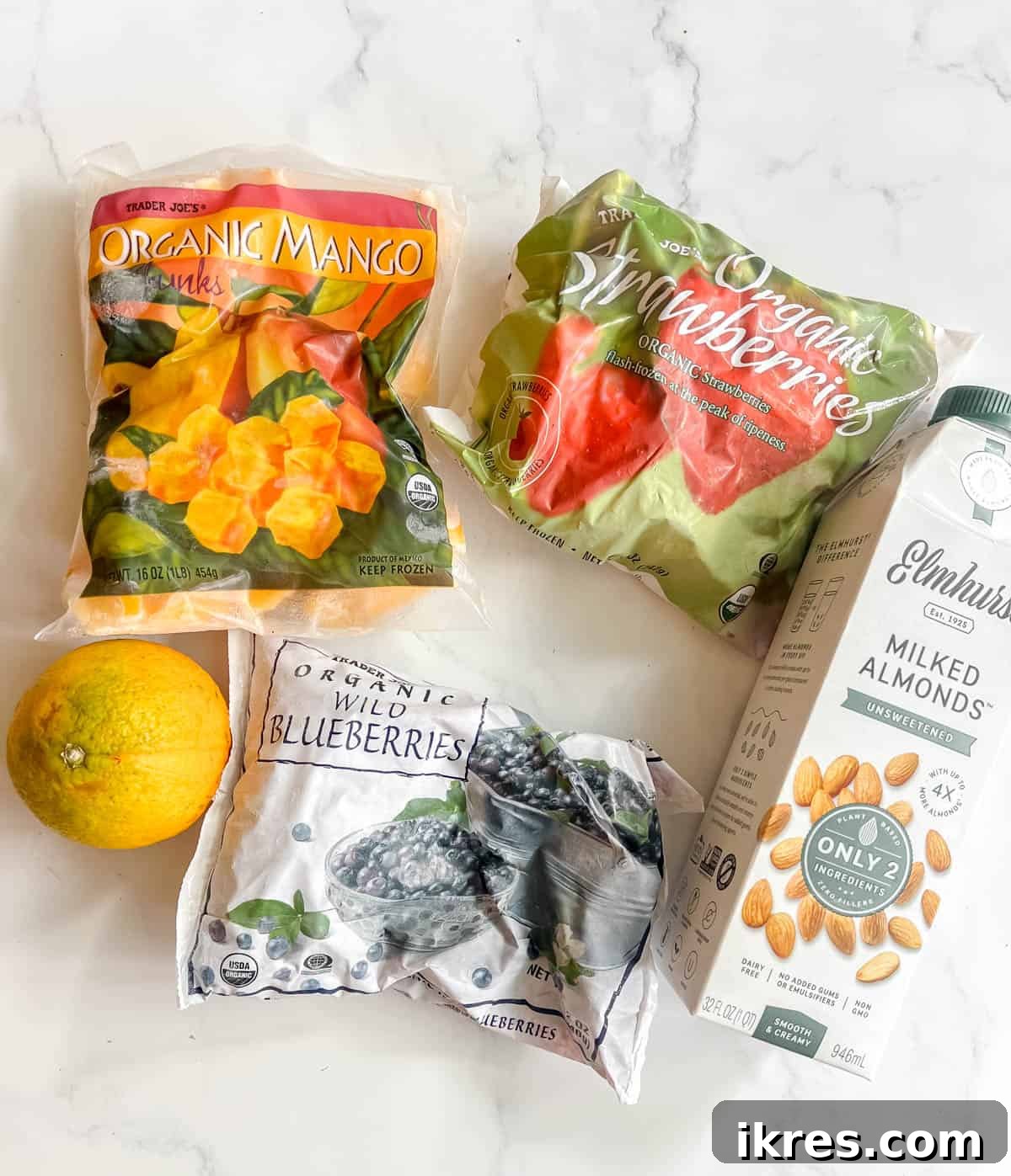 A selection of fresh and frozen ingredients laid out for making the dragon fruit powder smoothie, including mango, blueberries, strawberries, orange, and a jar of dragon fruit powder.