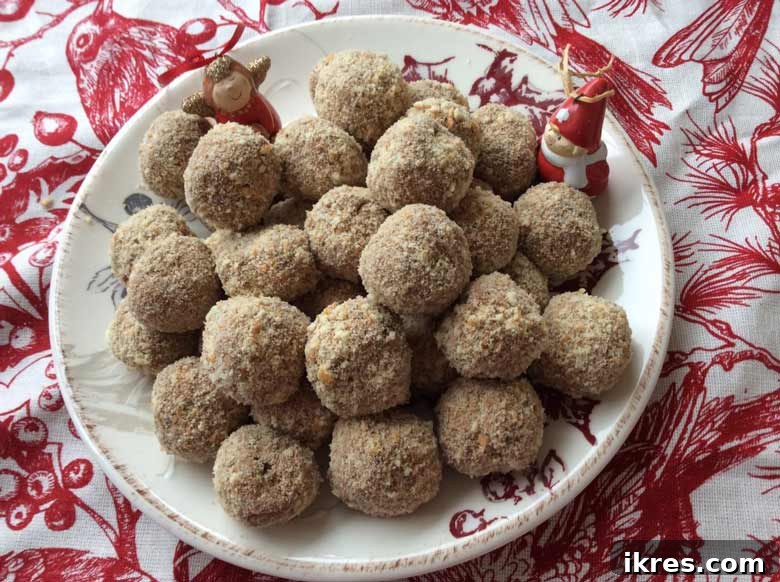 Decadent Chocolate Mousse Bites 2 Decadent chocolate mousse balls dusted with crushed vanilla wafers, beautifully arranged on a white plate with festive Christmas decorations in the background, ready for holiday serving.