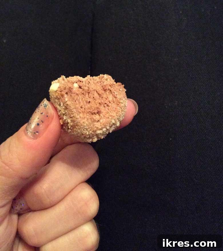 Decadent Chocolate Mousse Bites 6 A perfectly rolled chocolate mousse ball being coated thoroughly in a bowl of fine Nilla Wafer crumbs, demonstrating the final step before chilling.