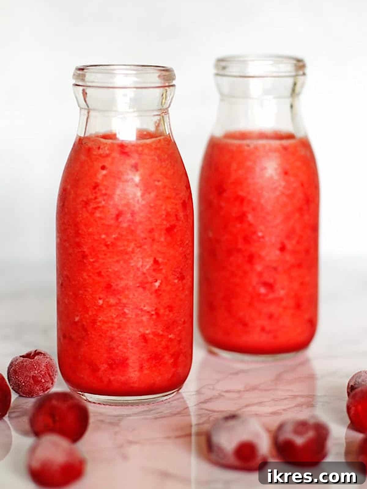 Tropical Cherry Pineapple Bliss 2 Two clear glasses filled with vibrant red Cherry Pineapple Smoothies, garnished with fresh cherries and pineapple chunks on a wooden counter. Frozen cherries and pineapple pieces are scattered nearby, highlighting the fresh ingredients used.