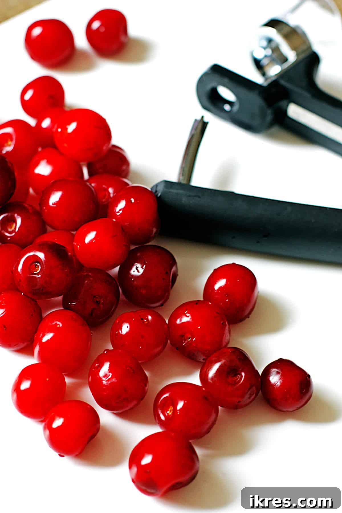 Tropical Cherry Pineapple Bliss 4 A collection of fresh tart cherries and a cherry pitter arranged neatly on a clean white kitchen counter, illustrating the simple process of preparing cherries for consumption or recipes.