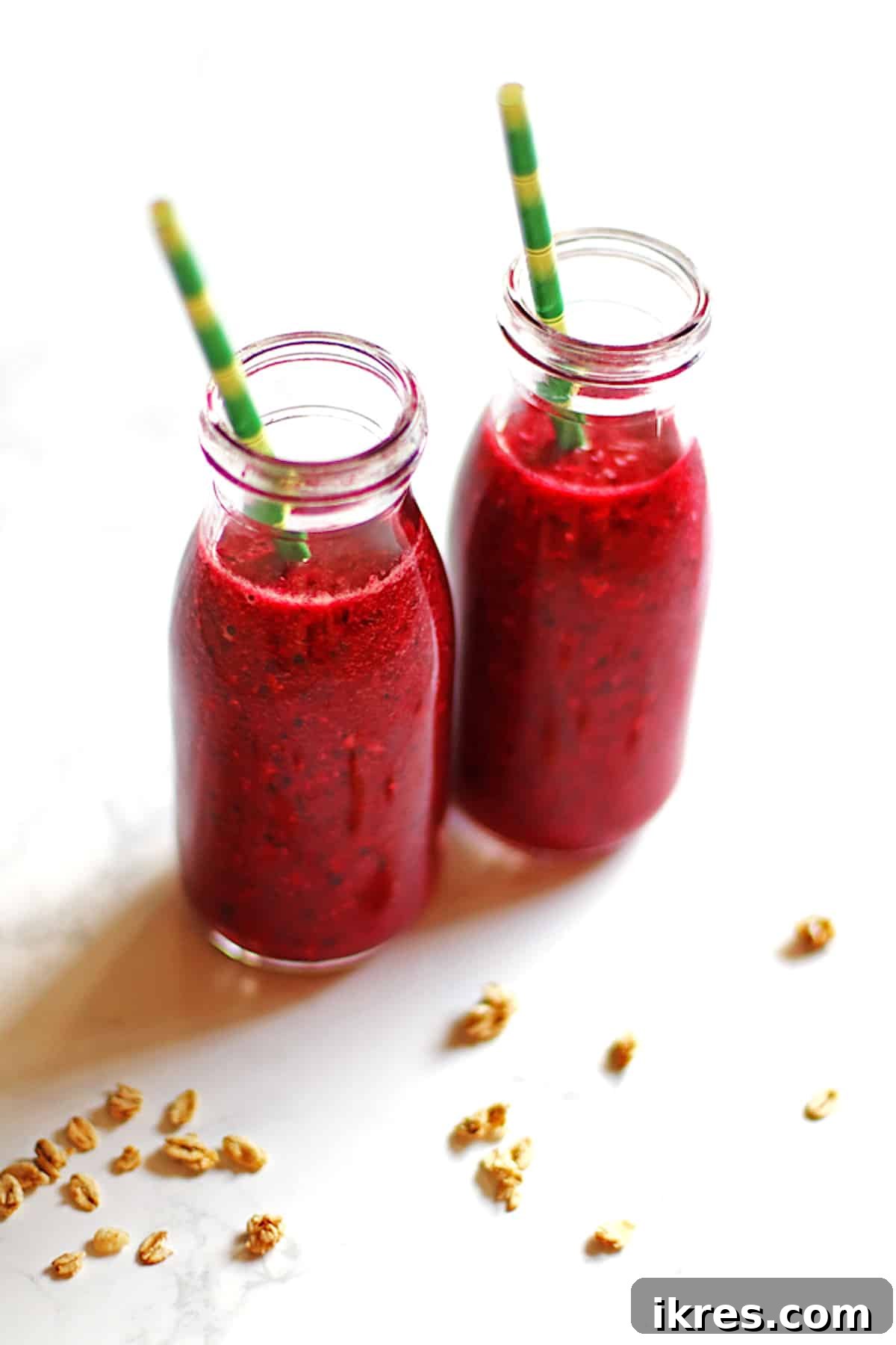Tropical Cherry Pineapple Bliss 5 Two small, clear bottles filled with a vibrant cherry pineapple smoothie, each adorned with a green and yellow straw, resting on a rustic wooden surface, ready for enjoyment.