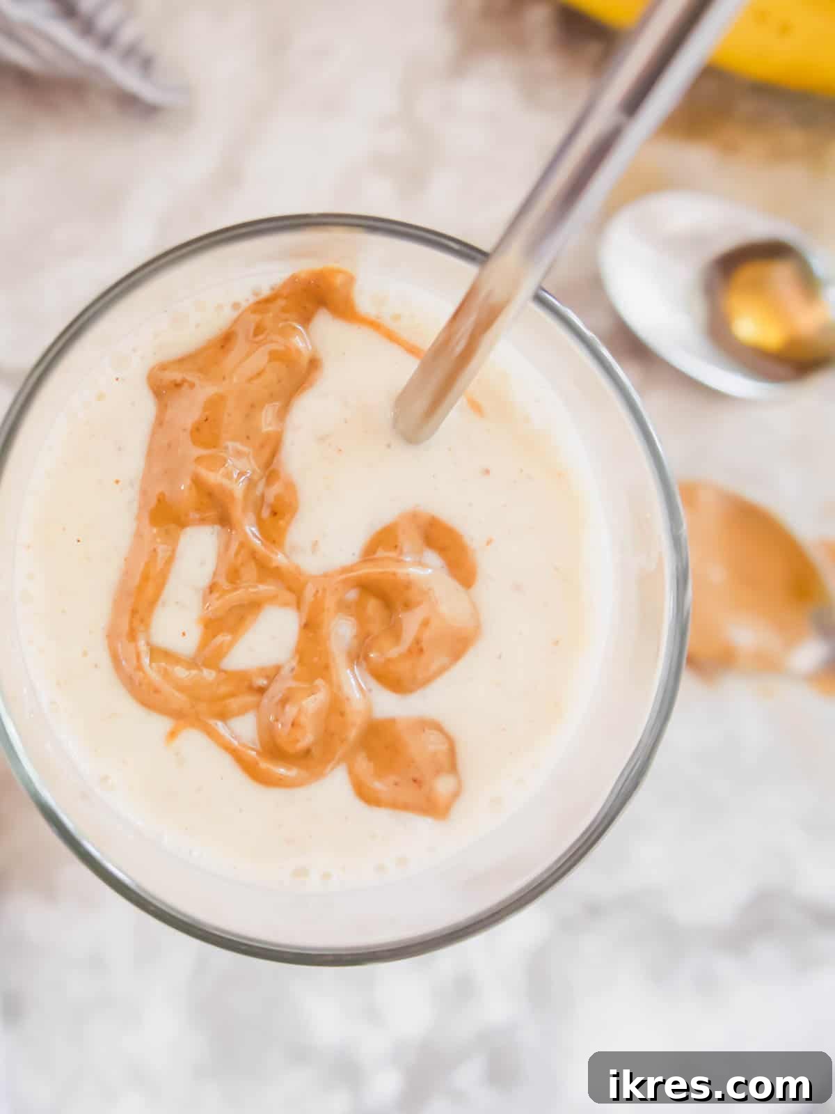 A close-up shot of a creamy banana yogurt smoothie, beautifully drizzled with natural almond butter on top, showcasing its delicious texture and garnish.