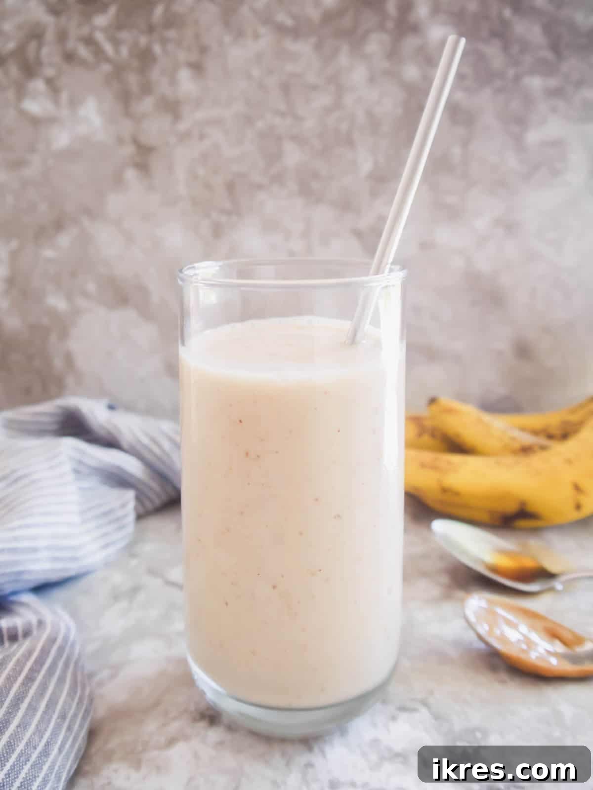A freshly blended banana maple smoothie poured into a clear glass, complete with a straw and a vibrant green background, ready for immediate enjoyment.