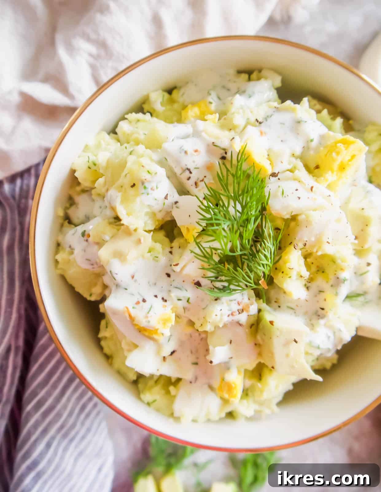 A large bowl of creamy dill ranch potato salad with avocado and eggs, ready to be served.