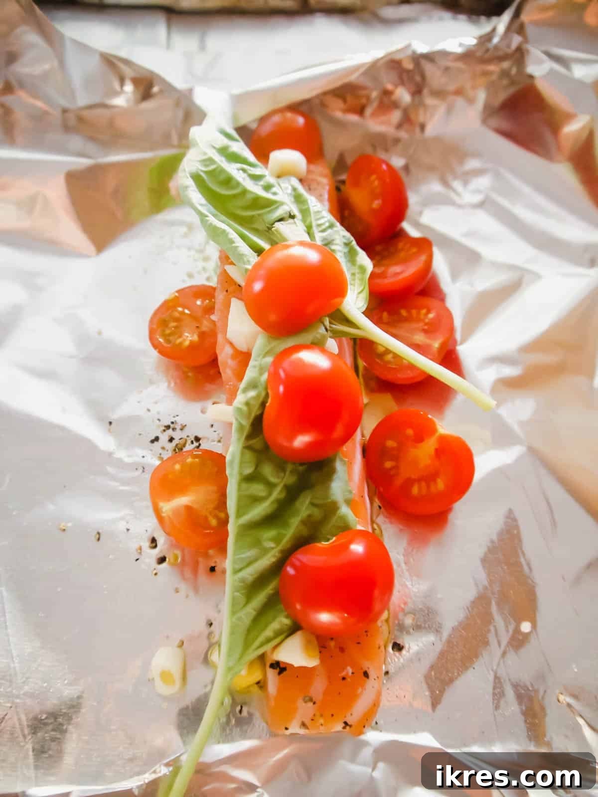 Basil Tomato Salmon Foil Packets 7 Salmon with garlic, basil, and sliced cherry tomatoes on top, ready to be wrapped.