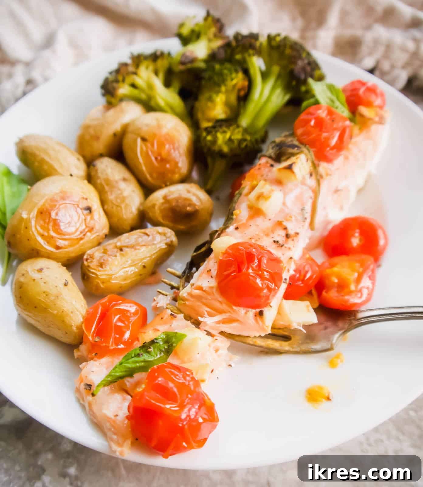 Basil Tomato Salmon Foil Packets 9 Baked salmon with tomatoes on a plate with potatoes and broccoli, garnished with basil.