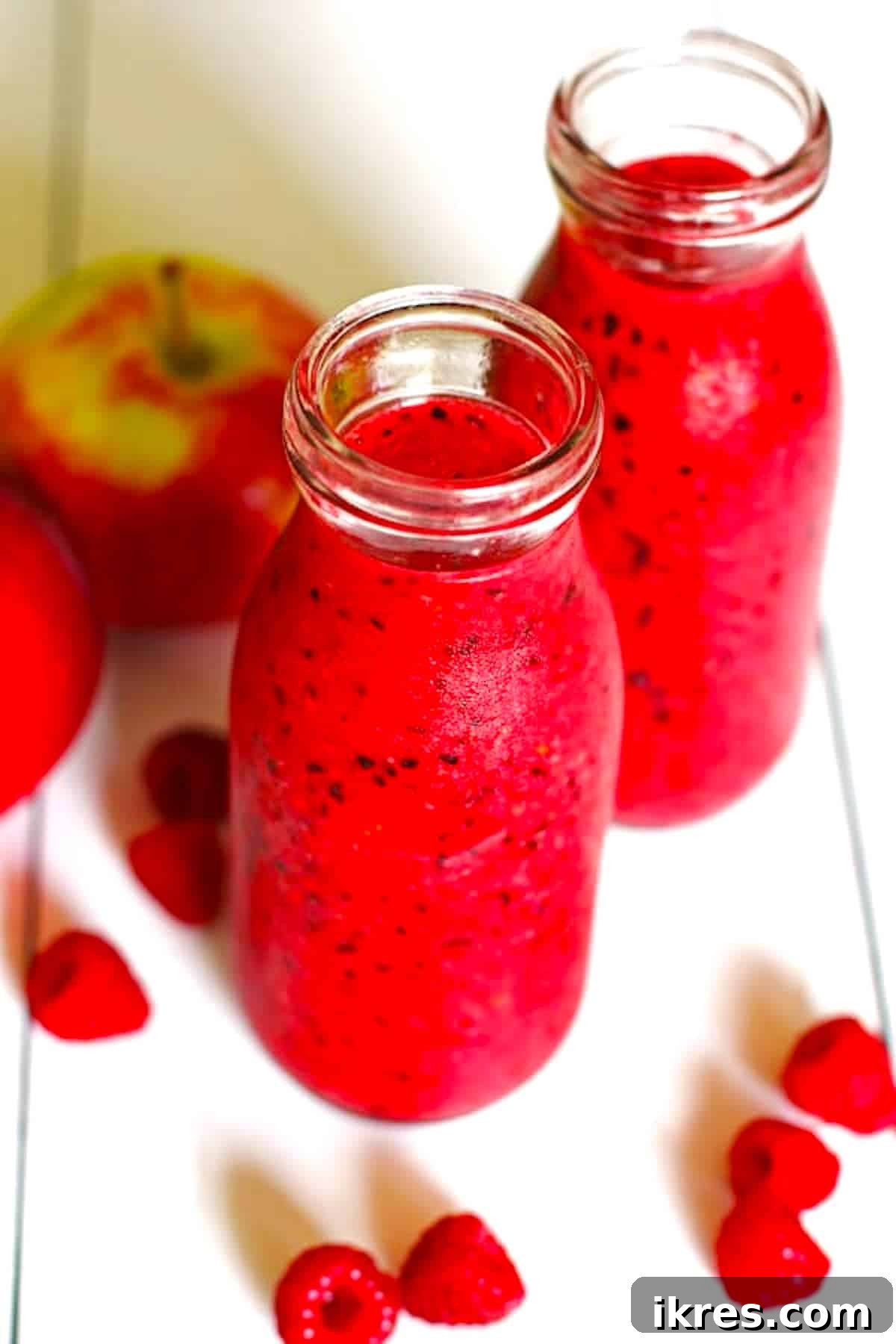 Berry Orchard Smoothie 6 A vibrant red smoothie, made from apples and berries, served in a clear glass on a clean white table.