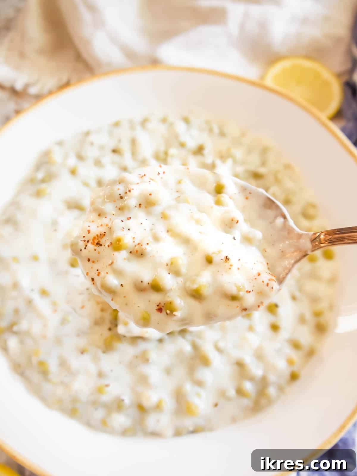 A spoon scooping up a generous portion of creamy, nutmeg-scented creamed peas from a serving bowl.