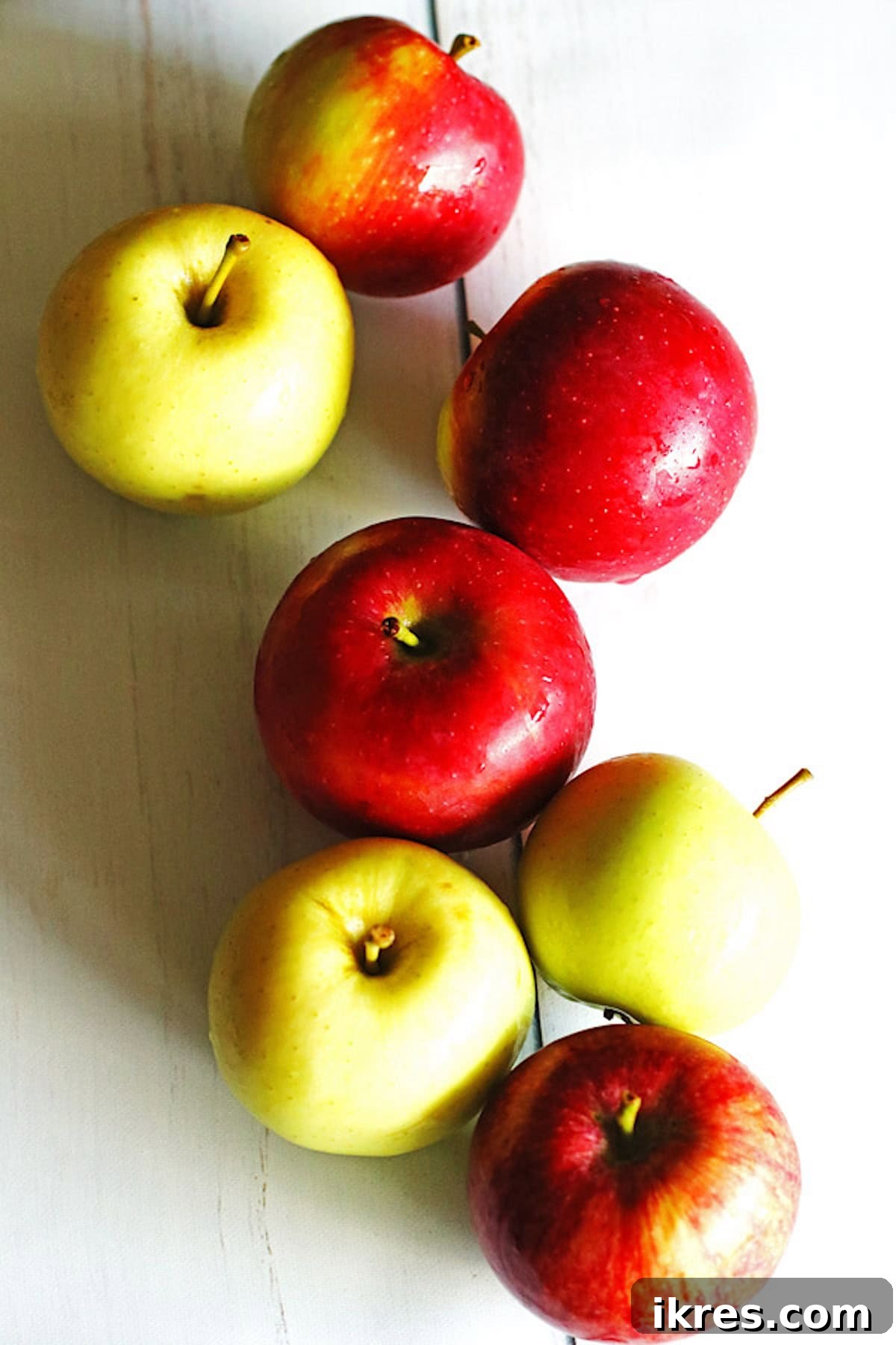 Golden Apple Cinnamon Flapjacks 3 Red and green apples on a white table, ready for baking.