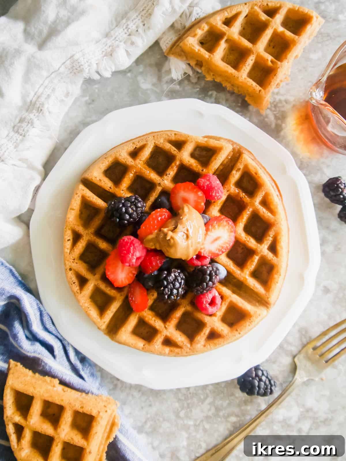 Paleo waffle on a plate with fresh fruit and maple syrup on top, ready to be enjoyed.