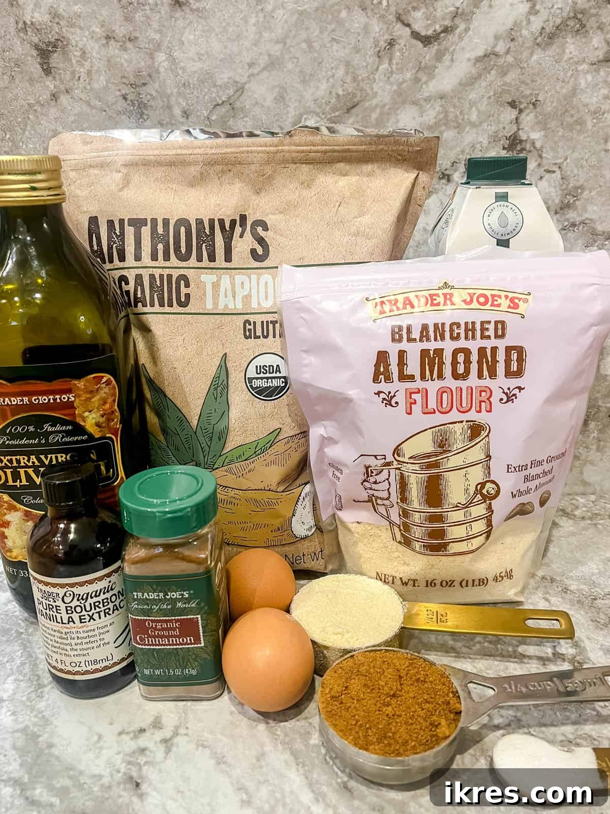 A collection of raw ingredients laid out on a wooden surface, including flours, eggs, oil, milk, and spices, all set to make the Paleo waffle recipe.