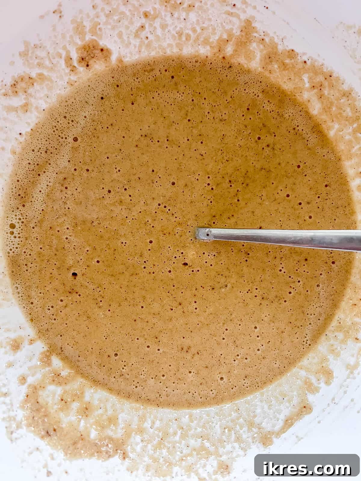 The wet egg yolk mixture being poured into the bowl containing the dry waffle ingredients.