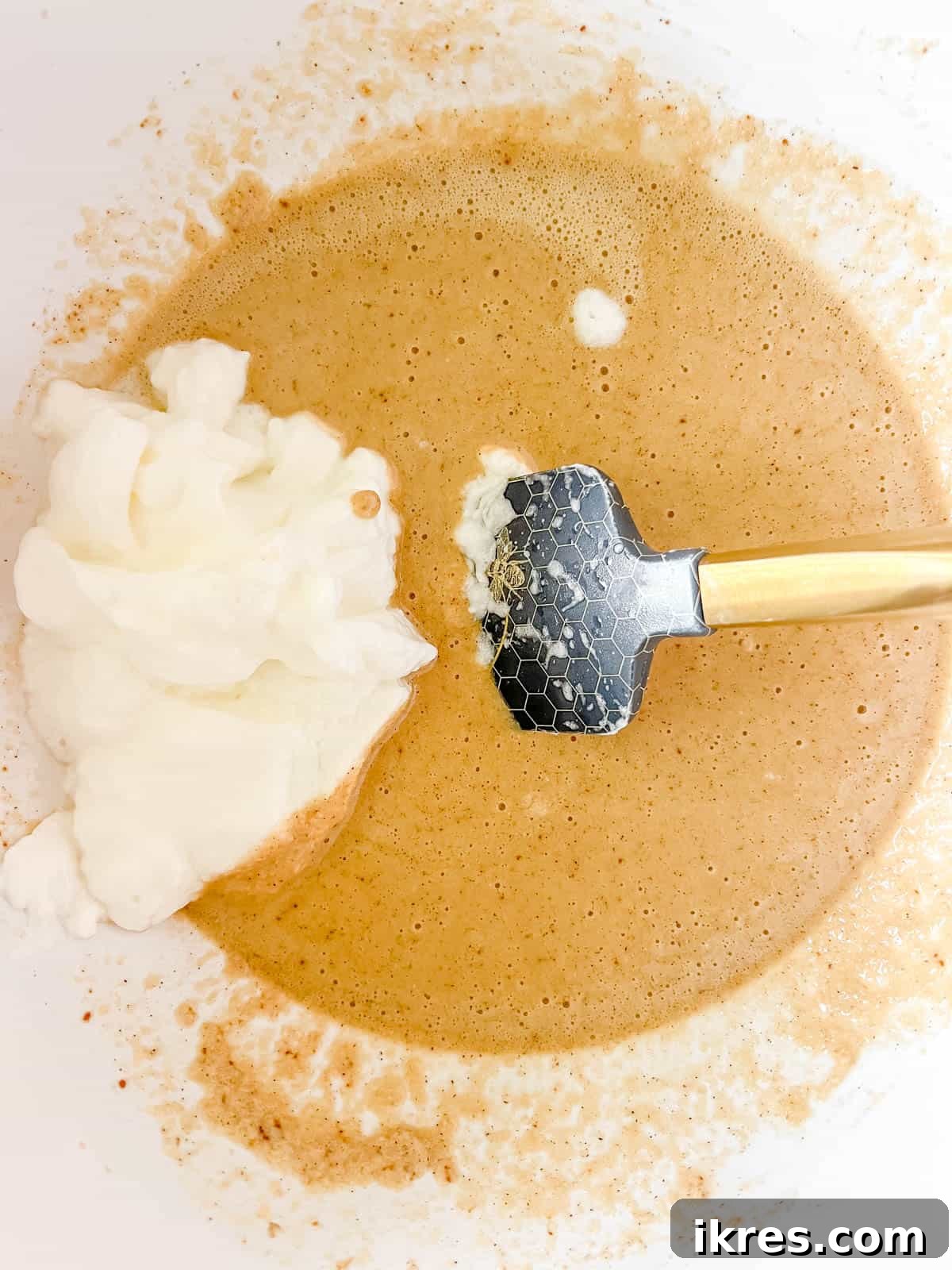Stiffly beaten egg whites being carefully added to the waffle batter.