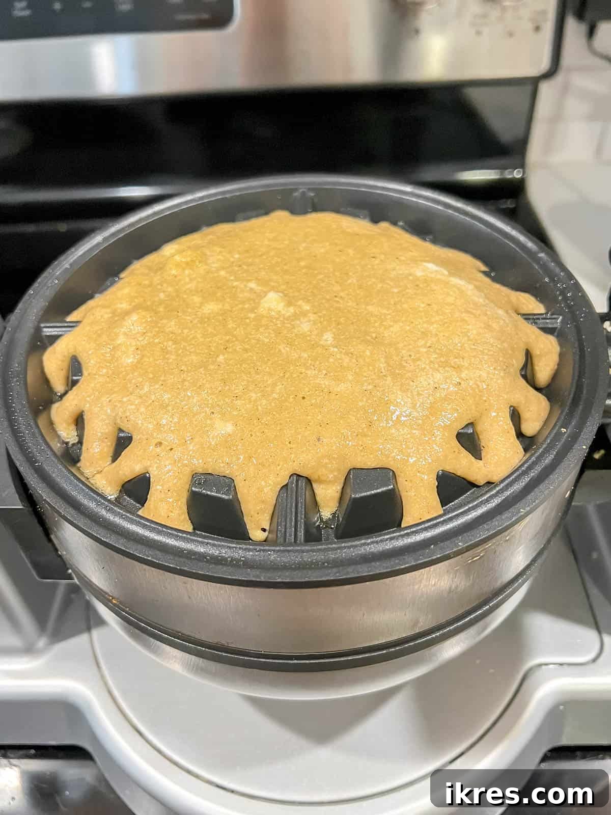 Paleo waffle batter being carefully poured onto a preheated waffle maker.
