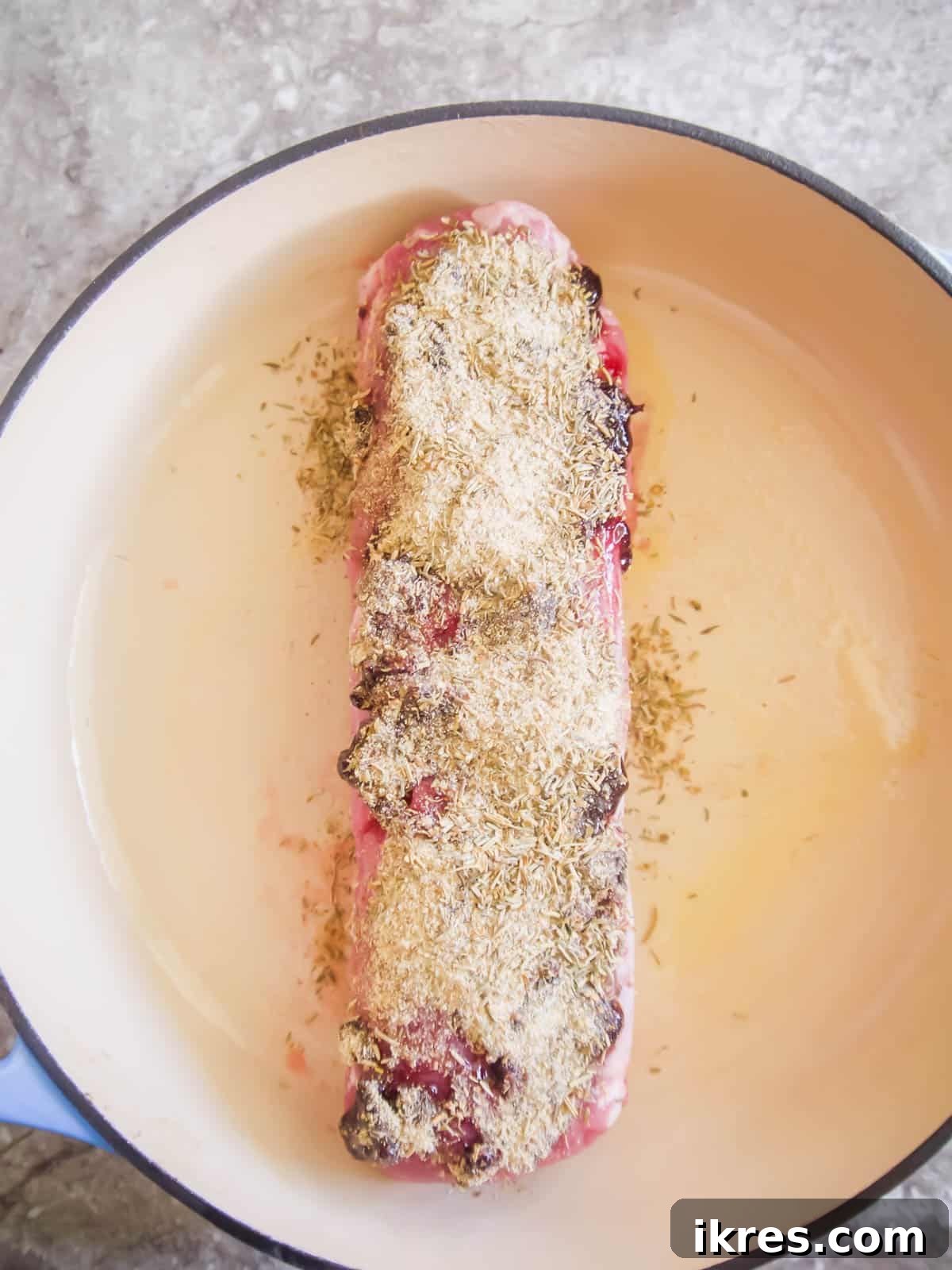 Dutch Oven Roasted Pork Loin with Sticky Spiced Fruit Glaze 6 The jam-coated pork loin in the Dutch oven being topped with a mixed spice blend, pressed gently to adhere.