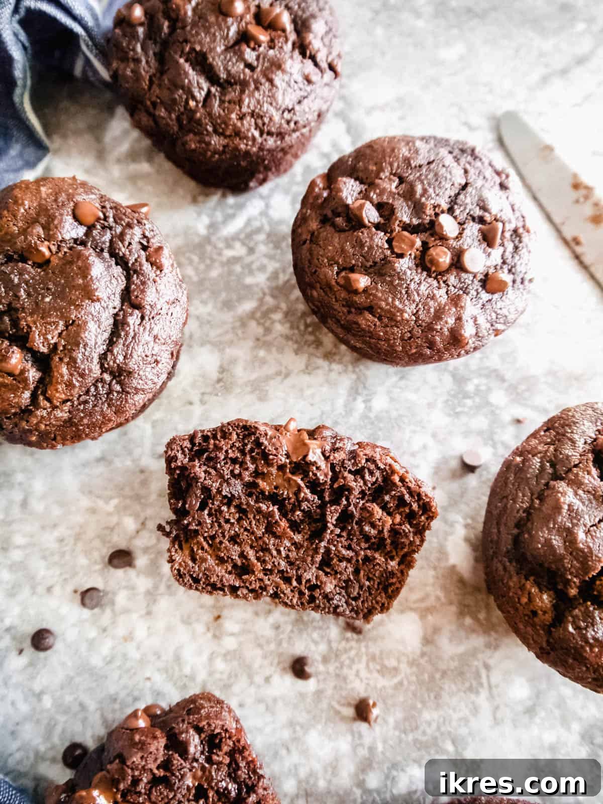 Wholesome Double Chocolate Banana Muffins Paleo Dairy Free Gluten Free 10 Banana chocolate gluten free muffins on a table, with one muffin cut in half to show the inside.