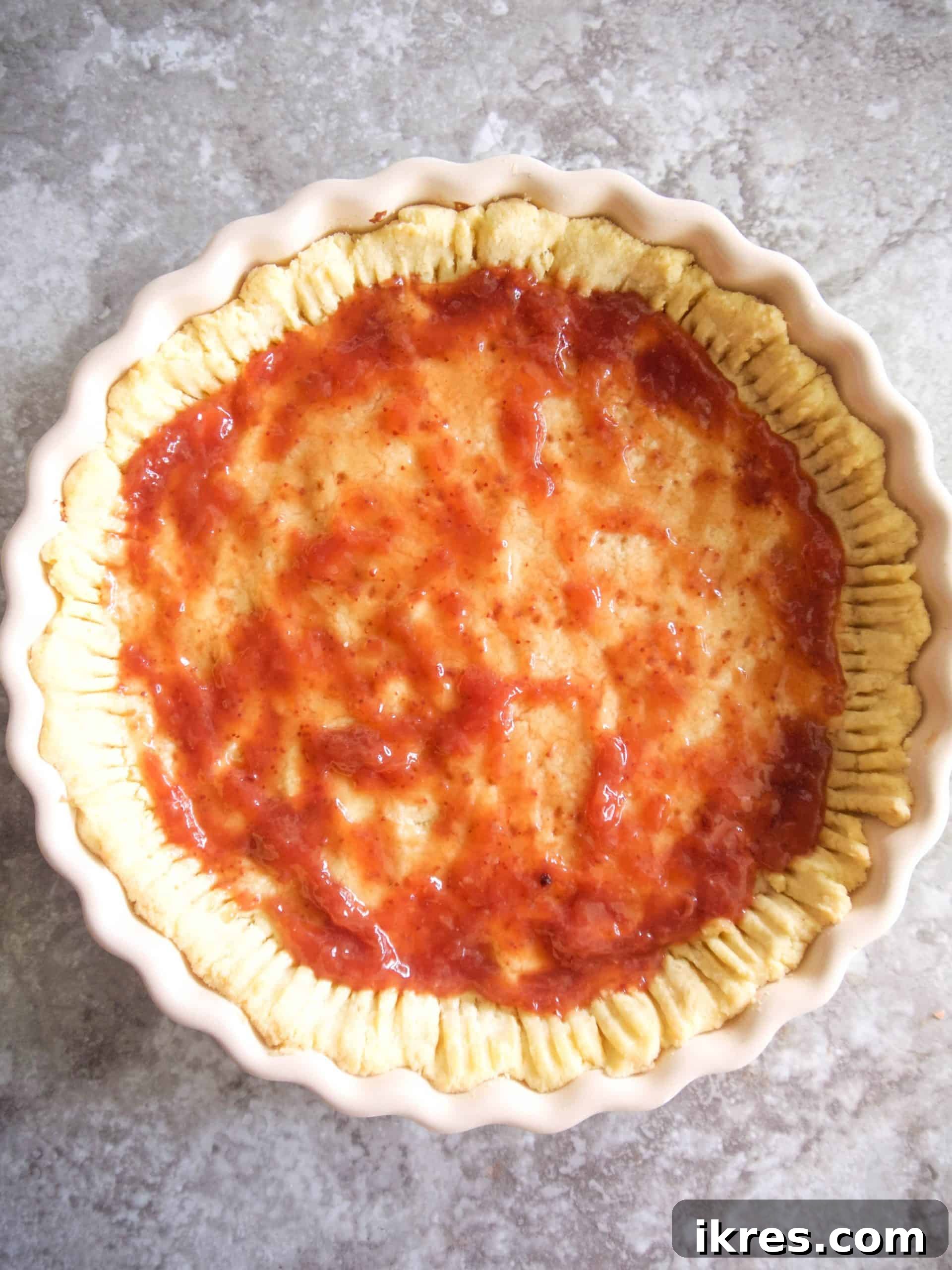 A smooth layer of strawberry jam spread over the partially baked tart crust.