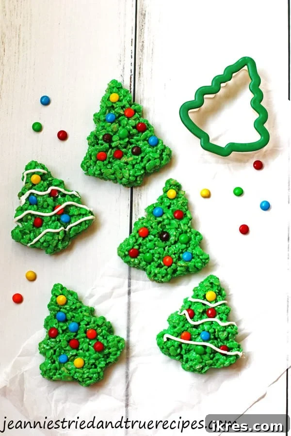 Vibrantly green, tree-shaped Rice Krispie Treats adorned with colorful M&M candies and delicate white icing resembling snow, arranged festively.