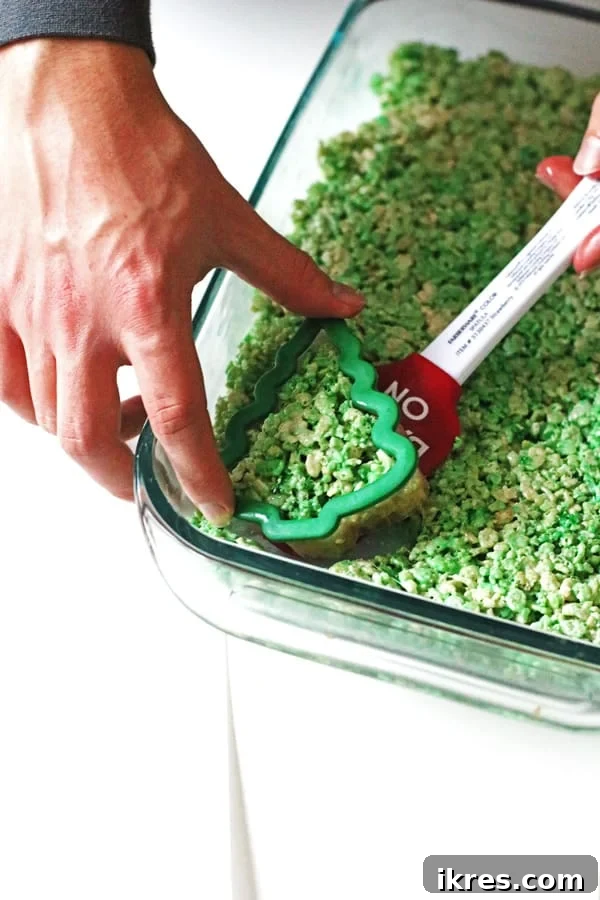 A Rice Krispie Christmas tree treat being carefully removed from the baking pan using a spatula after being cut with a cookie cutter.