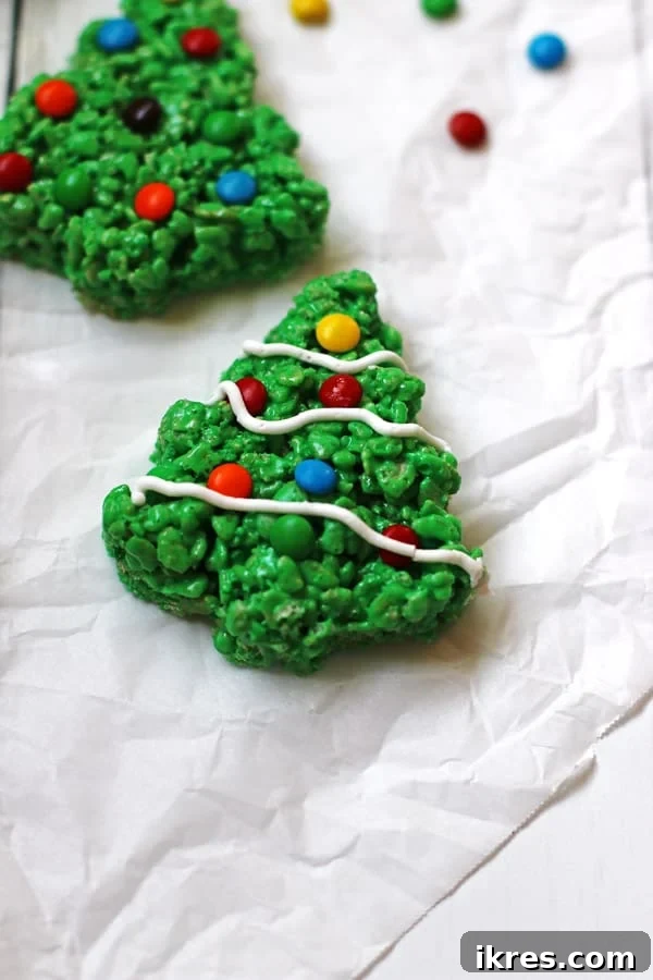 A display of tree-shaped Rice Krispie Treats, one of which is adorned with delicate white icing to resemble snow, enhancing its festive look.