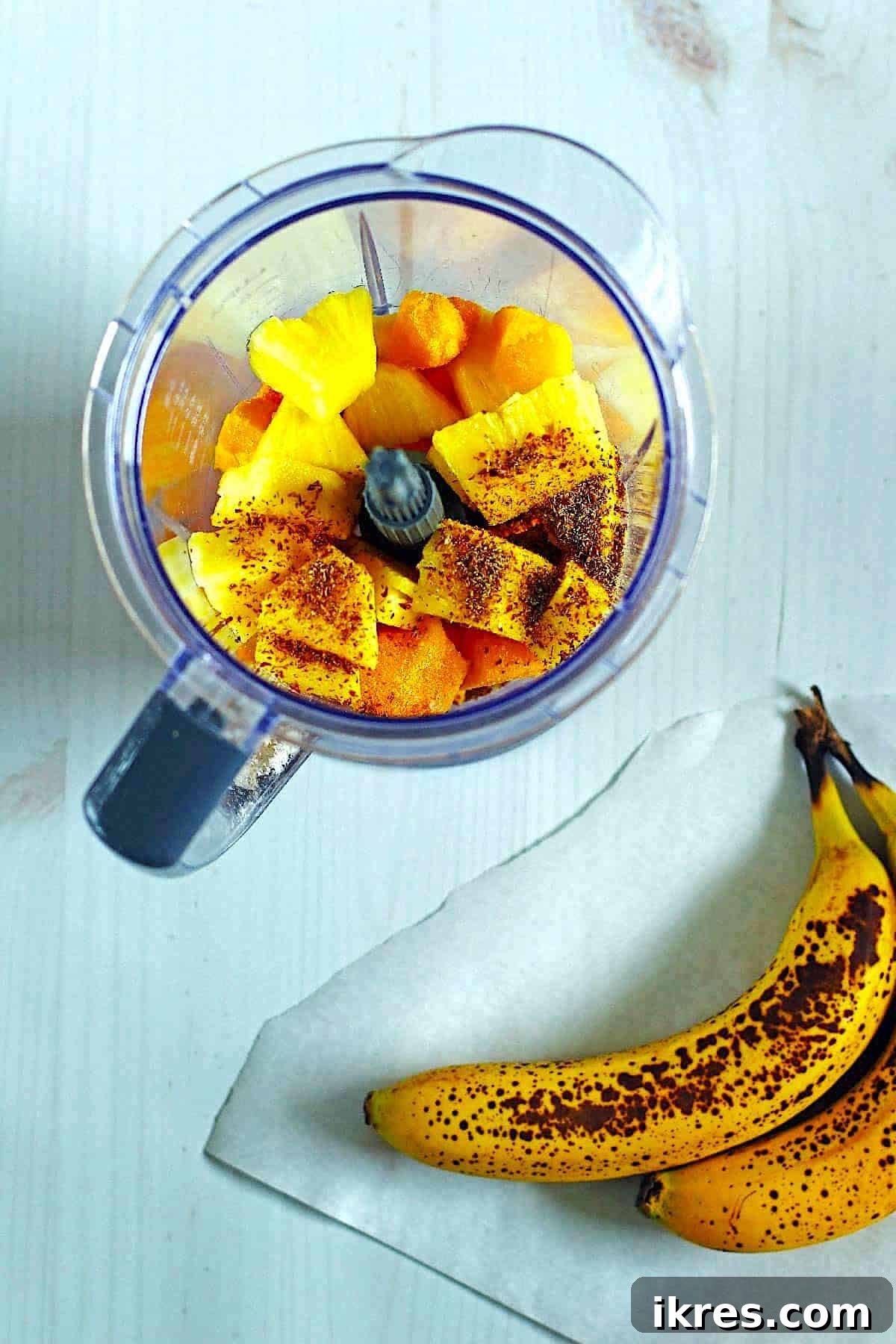 Smoothie ingredients ready in a blender, with ripe bananas placed beside it on a kitchen counter, highlighting the preparation stage.