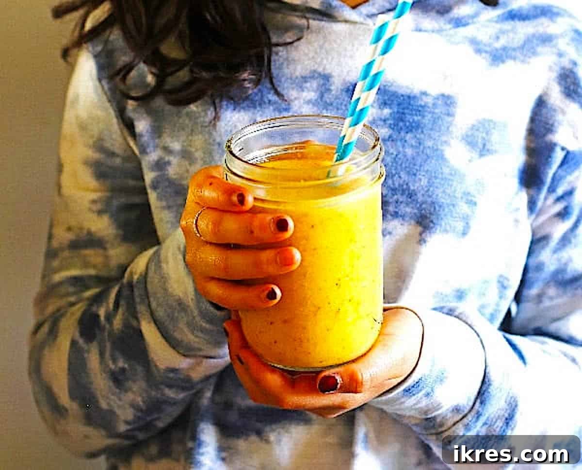 A young girl happily holding a canning jar filled with a healthy Pineapple Mango Smoothie, enjoying her refreshing drink.